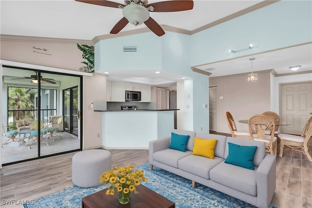 living room featuring ceiling fan with notable chandelier, light wood-type flooring, crown molding, and vaulted ceiling