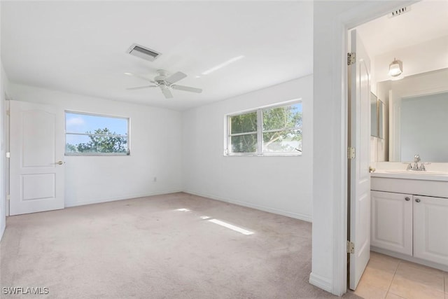 unfurnished bedroom featuring visible vents, ensuite bathroom, light carpet, a sink, and baseboards