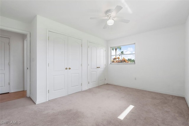 unfurnished bedroom featuring carpet floors, baseboards, a ceiling fan, and multiple closets