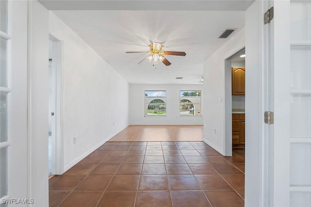 empty room featuring baseboards, dark tile patterned floors, visible vents, and a ceiling fan