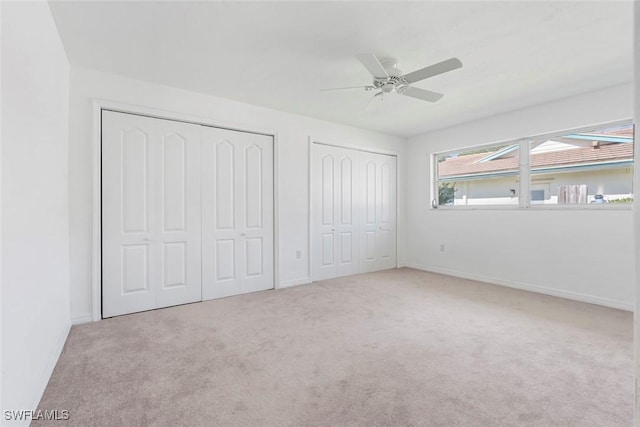 unfurnished bedroom with baseboards, ceiling fan, carpet, and multiple closets