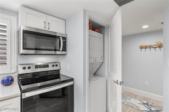 kitchen featuring appliances with stainless steel finishes, light hardwood / wood-style flooring, stacked washer and dryer, and white cabinets