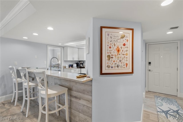 kitchen with a breakfast bar area, sink, light hardwood / wood-style flooring, white cabinets, and kitchen peninsula