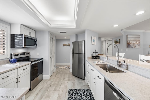 kitchen with appliances with stainless steel finishes, white cabinets, light wood-type flooring, light stone countertops, and sink