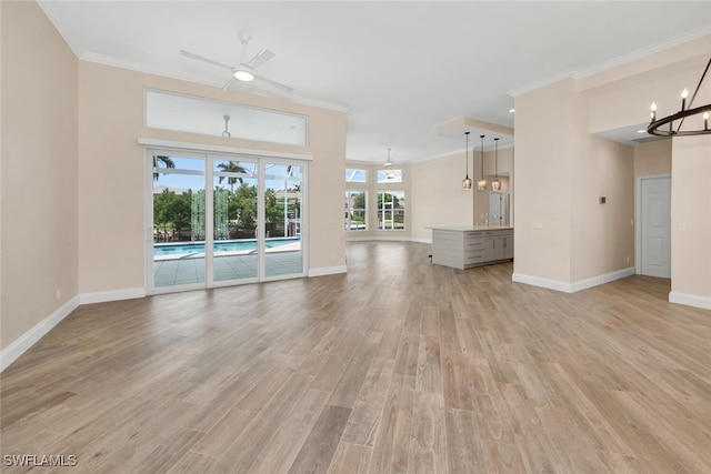 unfurnished living room featuring ceiling fan with notable chandelier, light wood-type flooring, and ornamental molding