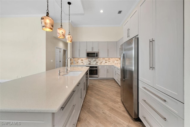 kitchen featuring stainless steel appliances, a center island with sink, decorative light fixtures, light wood-type flooring, and tasteful backsplash