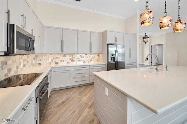 kitchen featuring stainless steel appliances, hanging light fixtures, decorative backsplash, sink, and light hardwood / wood-style flooring