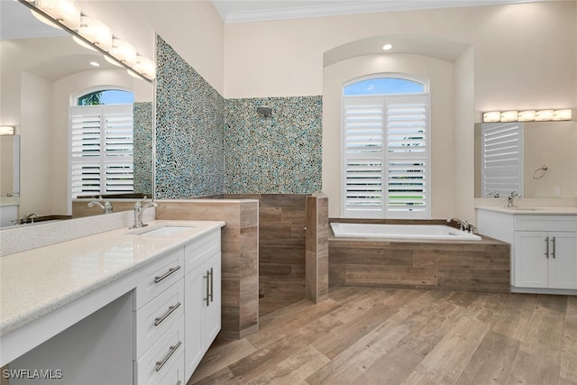 bathroom with tiled tub, dual bowl vanity, crown molding, and a healthy amount of sunlight