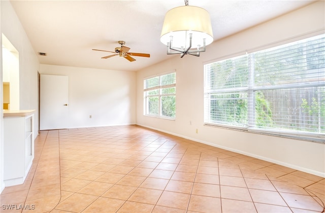 tiled empty room with ceiling fan with notable chandelier