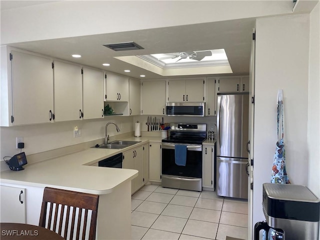 kitchen with a tray ceiling, stainless steel appliances, light countertops, visible vents, and a sink