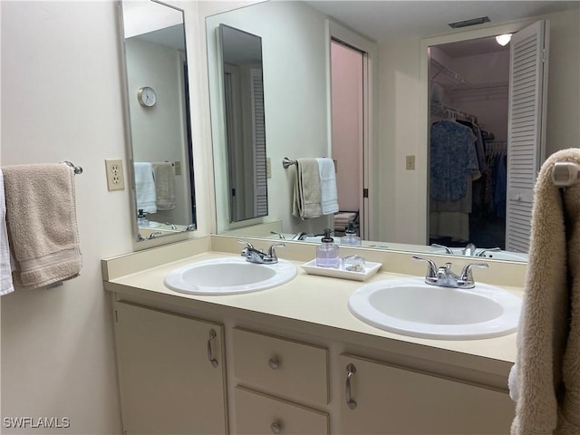 bathroom with visible vents, double vanity, a sink, and a walk in closet