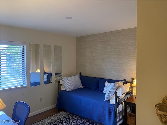 bedroom with an accent wall, baseboards, and wood finished floors