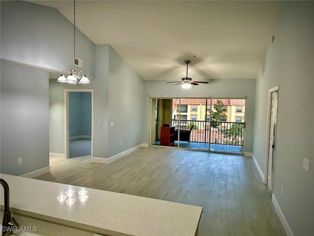 unfurnished living room with high vaulted ceiling, ceiling fan with notable chandelier, and hardwood / wood-style flooring