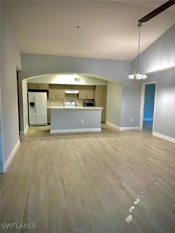 unfurnished living room with high vaulted ceiling, a chandelier, and light hardwood / wood-style flooring