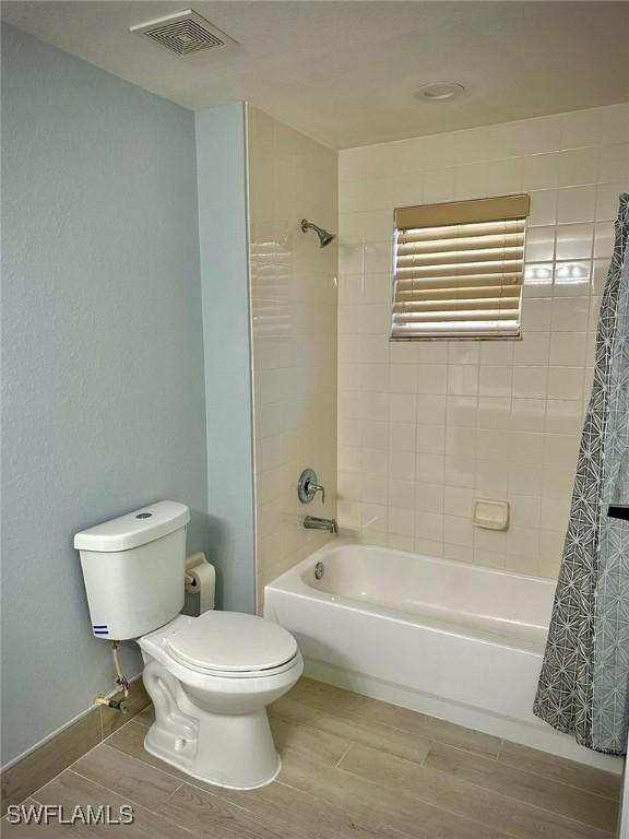 bathroom with shower / tub combo with curtain, hardwood / wood-style flooring, and toilet