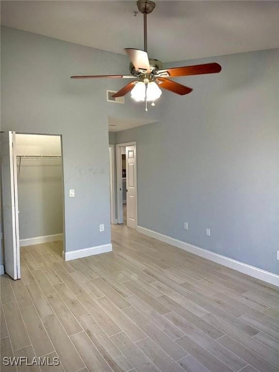 unfurnished bedroom featuring a walk in closet, light hardwood / wood-style flooring, a closet, and ceiling fan