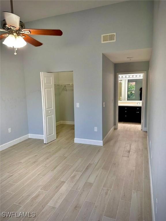 unfurnished bedroom with a closet, a walk in closet, ceiling fan, and light hardwood / wood-style flooring