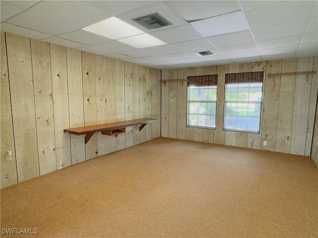 carpeted spare room featuring a paneled ceiling and wood walls