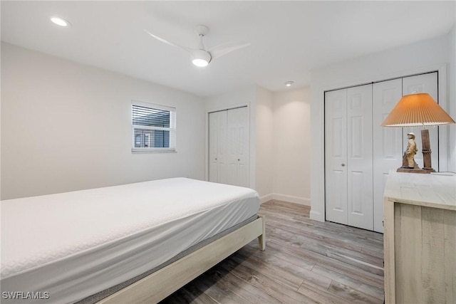 bedroom with light hardwood / wood-style floors, ceiling fan, and multiple closets