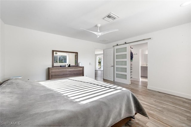 bedroom with ceiling fan, a barn door, ensuite bathroom, and light hardwood / wood-style flooring