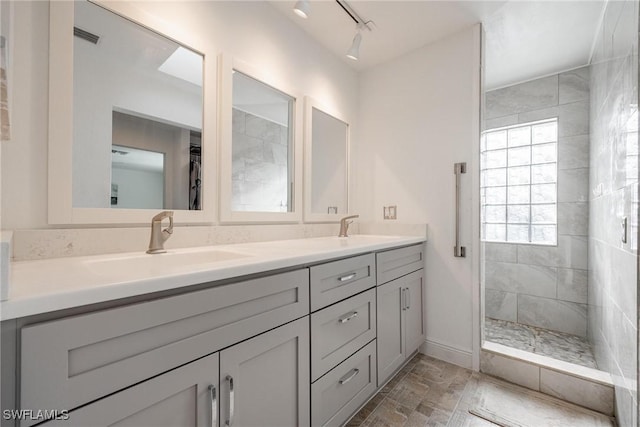 bathroom with tiled shower, vanity, and track lighting