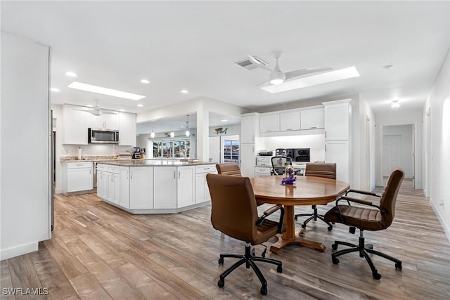 dining room featuring a skylight, light hardwood / wood-style flooring, and ceiling fan