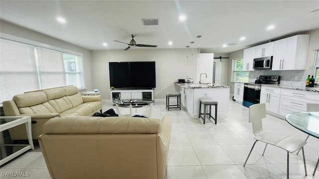 living room featuring ceiling fan, sink, a barn door, and light tile patterned floors