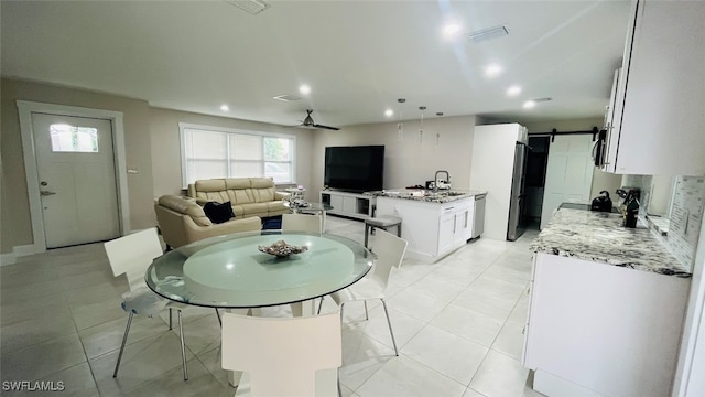 dining space with ceiling fan, light tile patterned flooring, sink, and a barn door