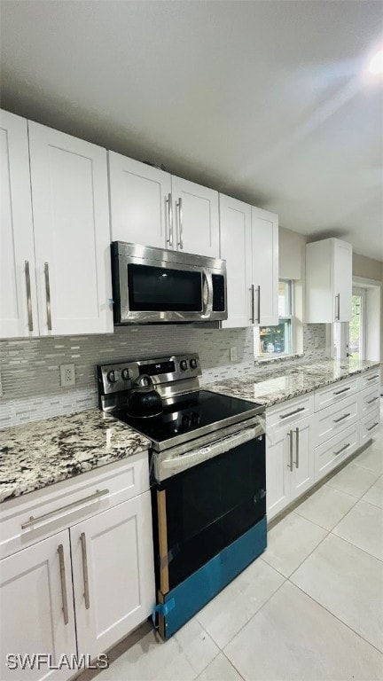 kitchen with tasteful backsplash, light stone counters, white cabinets, light tile patterned floors, and stainless steel appliances