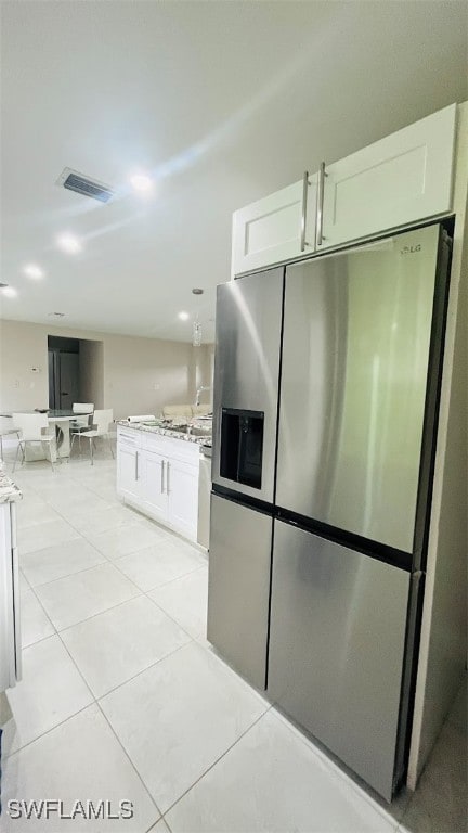 kitchen with stainless steel fridge, light tile patterned flooring, and white cabinetry