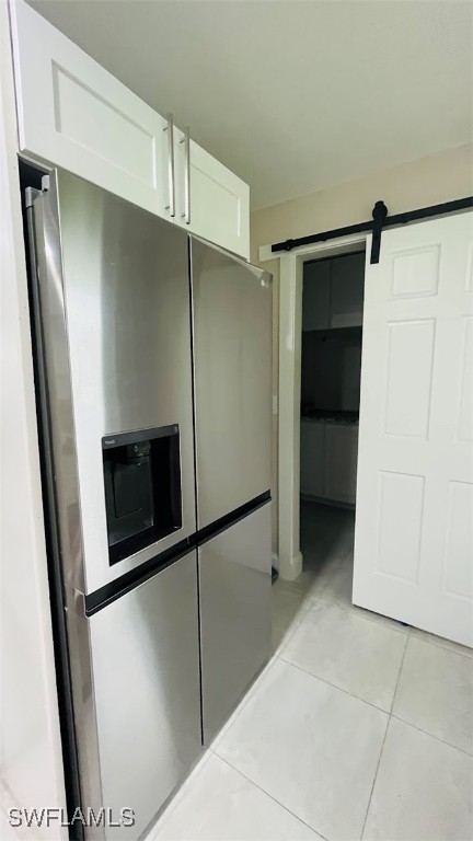 kitchen with stainless steel fridge, light tile patterned flooring, a barn door, and white cabinetry