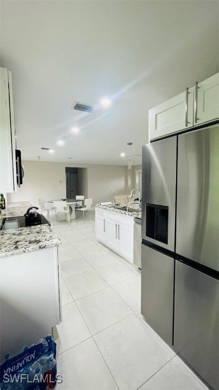 kitchen with light stone counters, white cabinetry, dishwashing machine, stainless steel fridge, and light tile patterned flooring