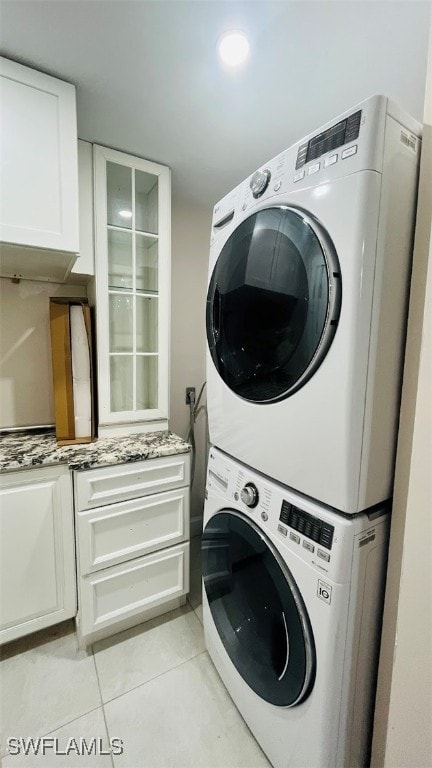 laundry room featuring light tile patterned floors, cabinets, and stacked washing maching and dryer