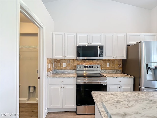 kitchen with tasteful backsplash, stainless steel appliances, light hardwood / wood-style floors, white cabinets, and vaulted ceiling