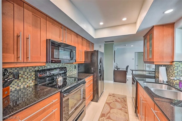 kitchen with dark stone counters, black appliances, light tile patterned floors, backsplash, and a tray ceiling