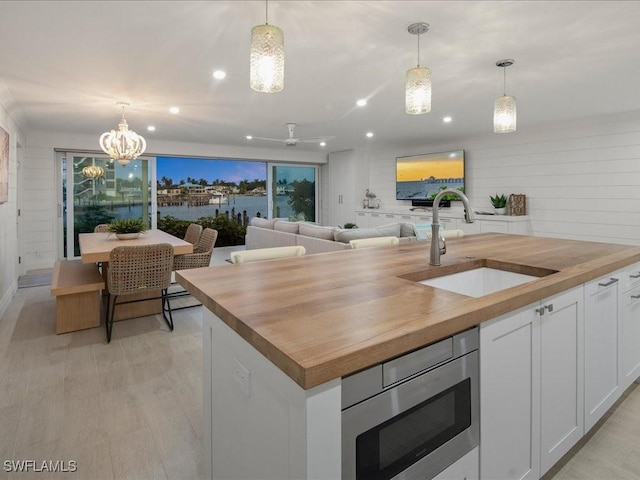 kitchen featuring wood counters, stainless steel microwave, sink, decorative light fixtures, and white cabinetry