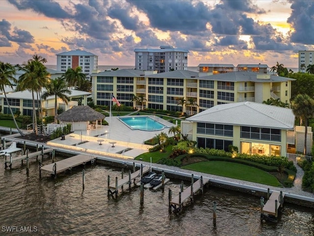 pool at dusk with a water view, a yard, and a dock