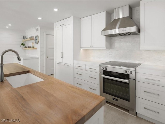 kitchen featuring stainless steel range, sink, wall chimney exhaust hood, tasteful backsplash, and white cabinets