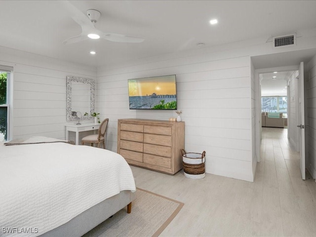 bedroom with ceiling fan, wooden walls, and light wood-type flooring