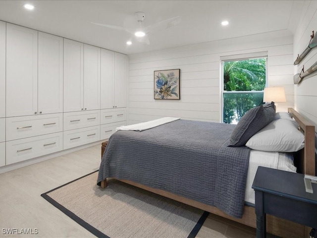 bedroom featuring wood walls, ceiling fan, a closet, and light hardwood / wood-style flooring