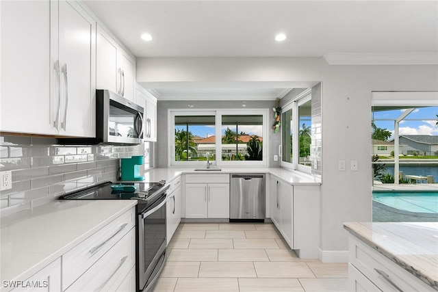 kitchen featuring a water view, stainless steel appliances, white cabinets, and ornamental molding