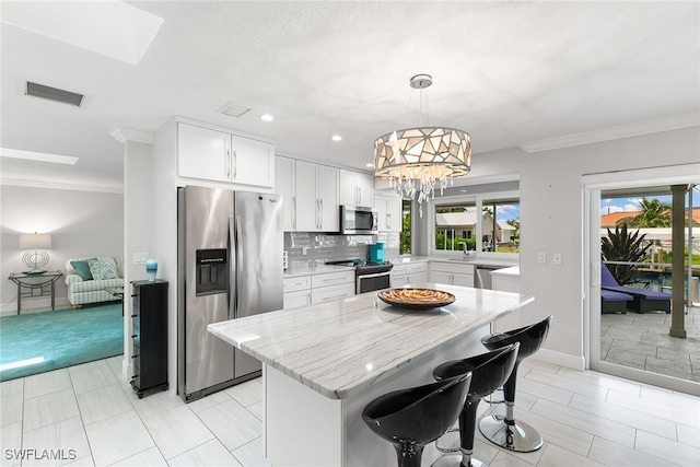 kitchen featuring appliances with stainless steel finishes, white cabinetry, a kitchen island, pendant lighting, and ornamental molding