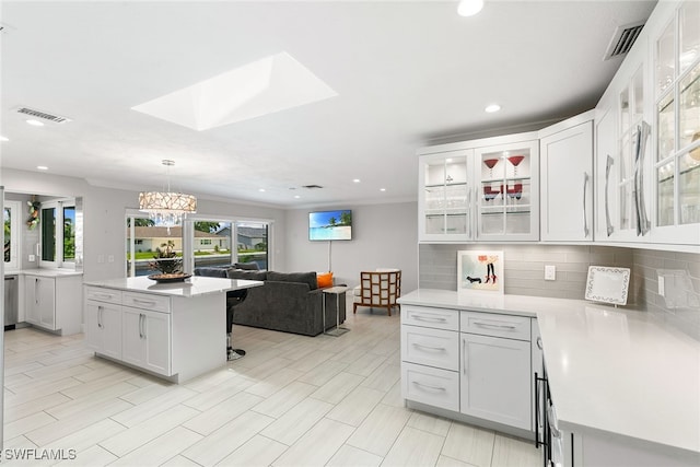 kitchen featuring a skylight, hanging light fixtures, tasteful backsplash, white cabinetry, and a notable chandelier