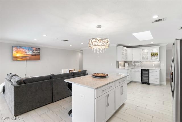 kitchen with white cabinets, beverage cooler, hanging light fixtures, a skylight, and stainless steel fridge