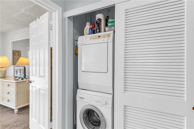 clothes washing area with hardwood / wood-style floors, a textured ceiling, and stacked washing maching and dryer