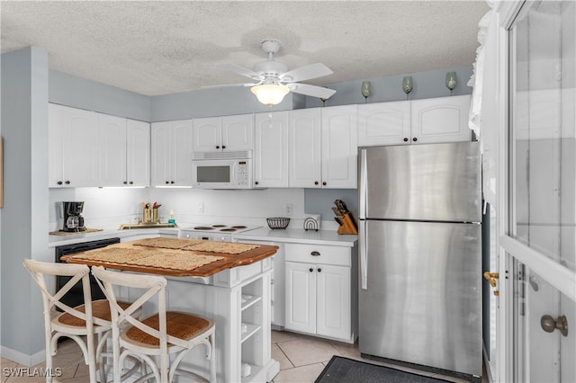 kitchen with a breakfast bar, stainless steel refrigerator, white cabinetry, light tile patterned floors, and a textured ceiling