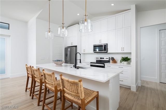 kitchen with an island with sink, hanging light fixtures, sink, white cabinetry, and appliances with stainless steel finishes