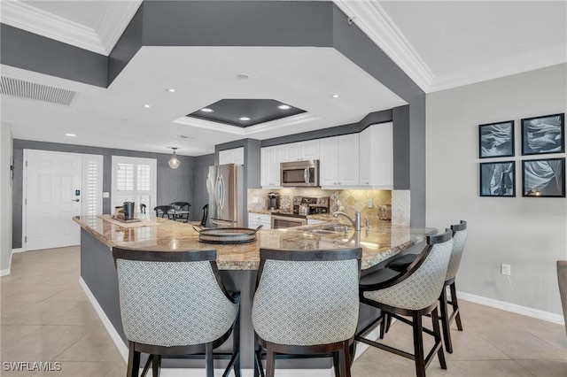 kitchen with a breakfast bar, visible vents, appliances with stainless steel finishes, white cabinets, and a peninsula