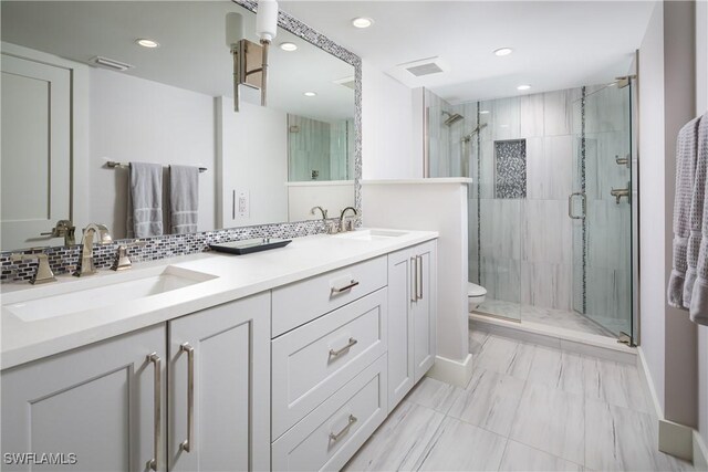 bathroom with dual bowl vanity, toilet, a shower with door, and backsplash