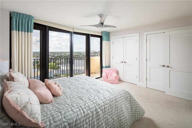 carpeted bedroom with a water view, access to outside, ceiling fan, and multiple closets